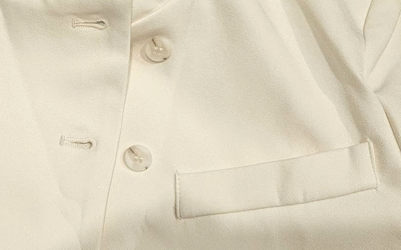 Close-up of the cream blazer's buttons and welt pocket